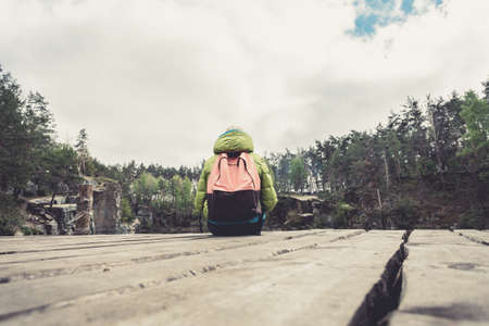 A female traveler is sitting on a wooden pier near a beautiful lake in a pine forest.の写真素材