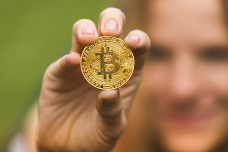 A woman holds a gold coin bitcoin in her handsの写真素材