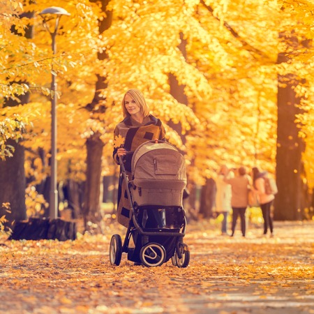 A young mother with a stroller walks through the autumn park