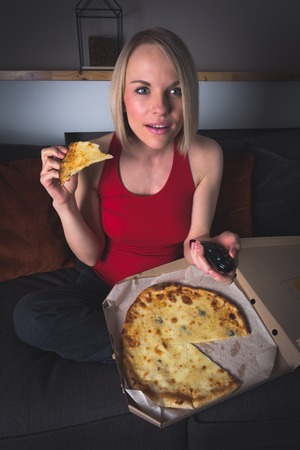 A woman watches TV and eats pizza in a dark room.の写真素材