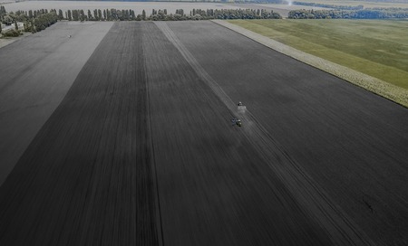 Two bright blue tractor plowing the ground against a black earth background.