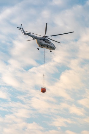 A fire fighter helicopter with a full basket of water flies against a beautiful skyの写真素材