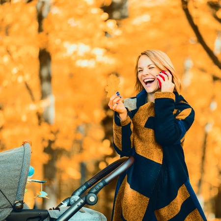 A young mother with a stroller is talking on her mobile phone while walking in the park