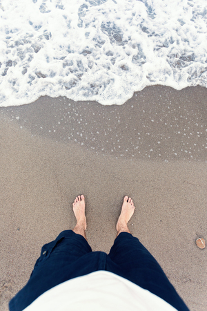 Blue waves in the sand with male feetの写真素材