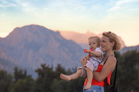 Young mother holding her little son in her arms against the backdrop of a mountain landscapeの写真素材
