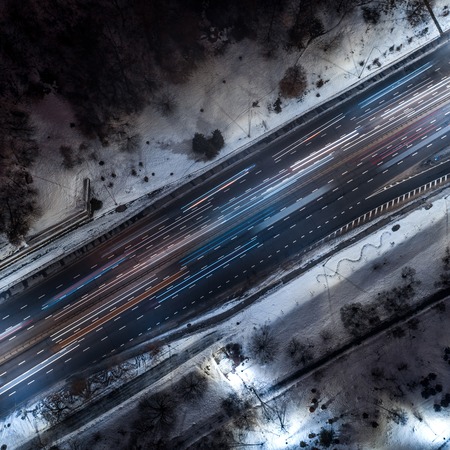 Top down view to night road with passing cars with headlights on between the winter park