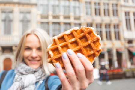 Young beautiful woman holding a traditional Belgian waffle on the background of the Great Market Square in Brussels, Belgiumの写真素材