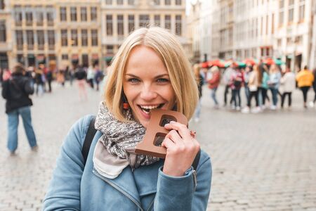 Woman tourist bites a bar of chocolate at the Grand Place in Brussels, Belgiumの写真素材