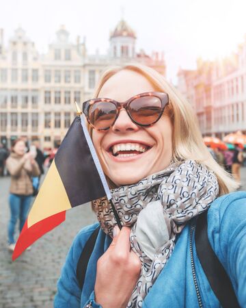 Woman tourist stands with the flag of Belgium on the background of the Grand-Place or the Grand Market Square in Brusselsの写真素材