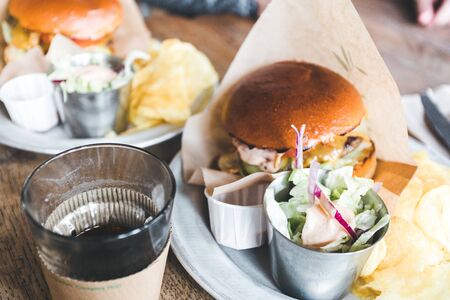 Craft beef burgers with vegetables on a plate with chips and salad on a wooden table.