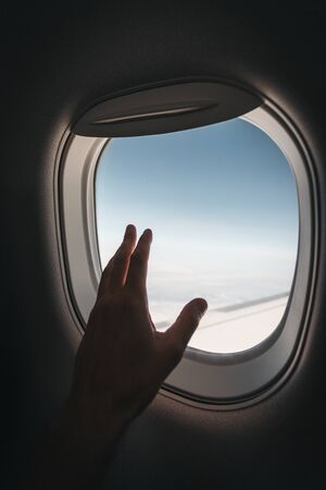 Porthole window in the plane with a mans hand during the flight.の写真素材