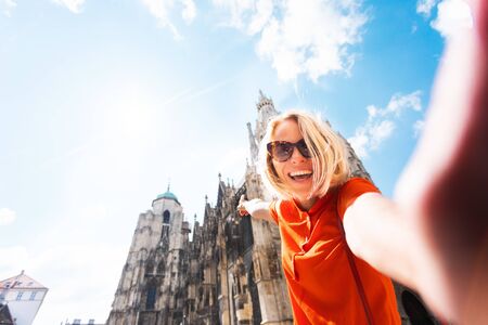 A young woman in a bright orange dress stands on the background of St. Stephens Cathedral in Vienna, Austriaの写真素材