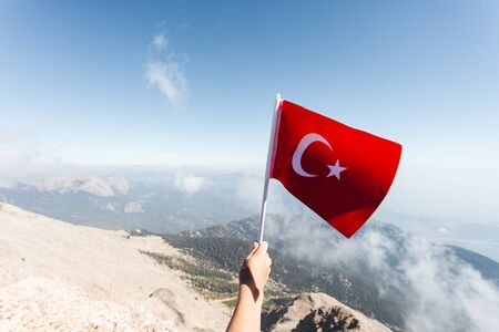 Turkey flag in a female hand against the backdrop of Taurus Mountains from a viewpoint of Tahtali Mountain. Tahtali Dagi, Antalya Province, Turkeyの写真素材