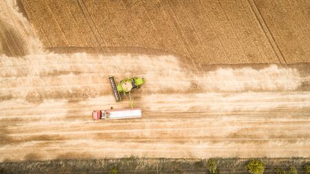 A beautiful new combine harvester dumps grain into a truck trailer on the field. Aerial viewの写真素材