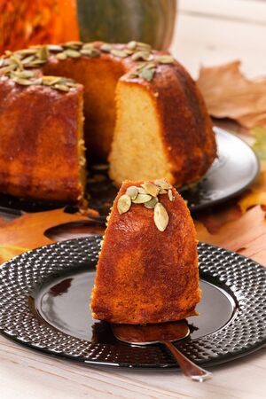 Pound pumpkin cake decorated with pumpkin seeds with a pumpkin in the background and a cut piece of cake on a separate plateの写真素材