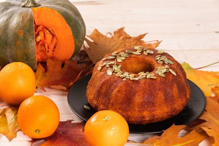 Bright autumn Pound pumpkin cake watered with orange syrup and garnished with pumpkin seeds on the background of autumn bright orange leaves.の写真素材