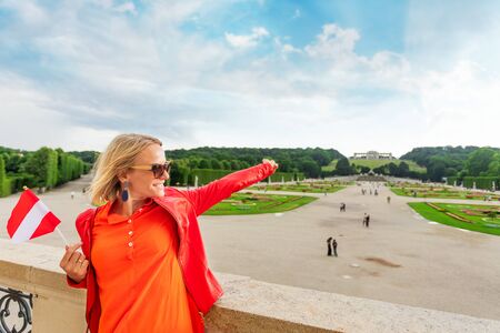 Young female tourist with the flag of Austria stands against a Schoenbrunn palace park in Vienna, Austriaのeditorial素材