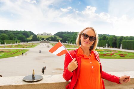 Young female tourist with the flag of Austria stands against a Schoenbrunn palace park in Vienna, Austriaのeditorial素材