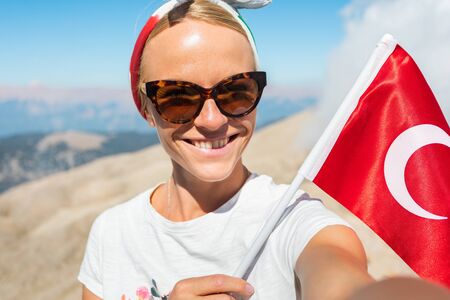 Young woman tourist stands on a viewing platform of Tahtali Mountain in Kemer with a red Turkey flag, Turkeyの写真素材