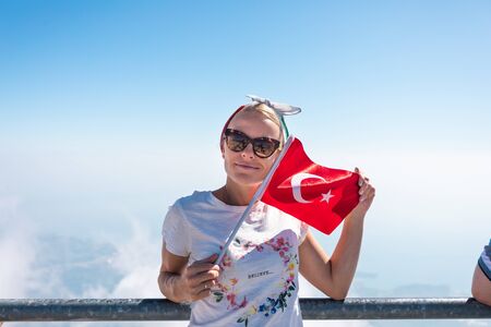 Young woman tourist stands on a viewing platform of Tahtali Mountain in Kemer with a red Turkey flag, Turkeyの写真素材