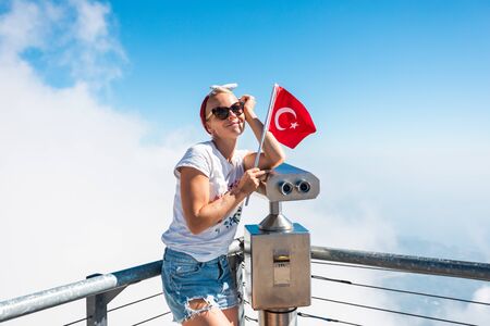 Young woman tourist stands on a viewing platform of Tahtali Mountain in Kemer with a red Turkey flag, Turkeyの写真素材