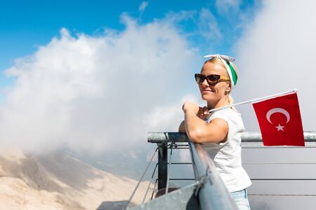 Young woman tourist stands on a viewing platform of Tahtali Mountain in Kemer with a red Turkey flag, Turkeyの写真素材