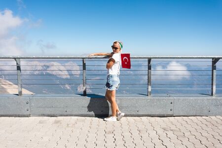 Young woman tourist stands on a viewing platform of Tahtali Mountain in Kemer with a red Turkey flag, Turkeyの写真素材