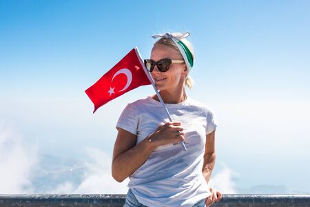 Young woman tourist stands on a viewing platform of Tahtali Mountain in Kemer with a red Turkey flag, Turkeyの写真素材