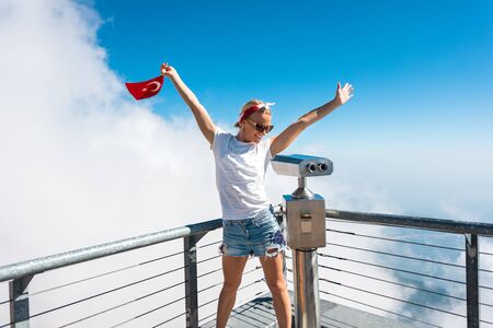 Young woman tourist stands on a viewing platform of Tahtali Mountain in Kemer with a red Turkey flag, Turkeyの写真素材