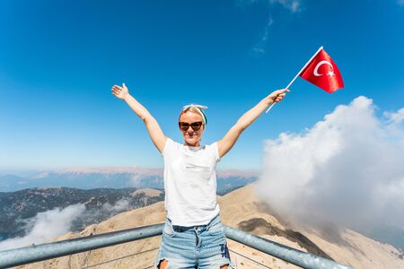 Young woman tourist stands on a viewing platform of Tahtali Mountain in Kemer with a red Turkey flag, Turkeyの写真素材