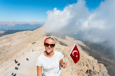 Young woman tourist stands on a viewing platform of Tahtali Mountain in Kemer with a red Turkey flag, Turkeyの写真素材