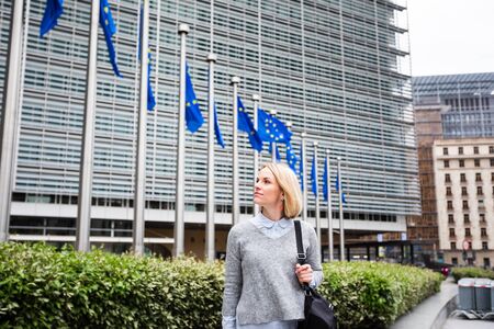 A young woman stands against the backdrop of the European Commission headquarters in Brussels, Belgiumの写真素材
