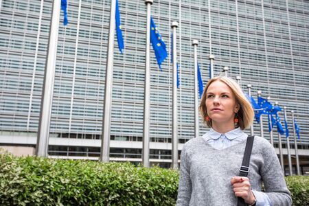 A young woman stands against the backdrop of the European Commission headquarters in Brussels, Belgiumの写真素材