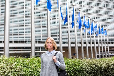 A young woman stands against the backdrop of the European Commission headquarters in Brussels, Belgiumの写真素材