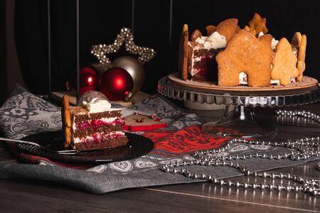 Cherry Cake Black forest on a dark background, decorated with gingerbread cookies with a cut piece on a serving plateの写真素材