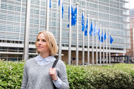 A young woman stands against the backdrop of the European Commission headquarters in Brussels, Belgiumの写真素材