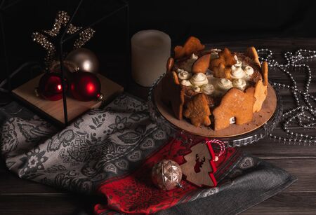Homemade Christmas cherry cake decorated with gingerbread cookies in a New Year's entourage on a dark background. Black Forest cake with cherries and sour cream on the background of Christmas tree toys.の写真素材