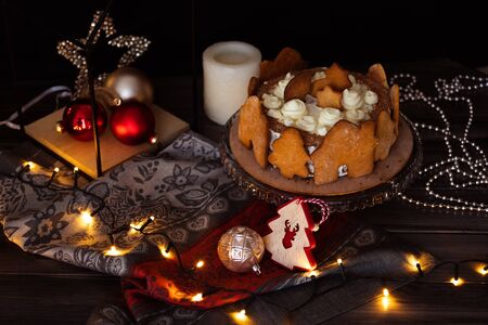 Black forest cherry cake decorated with gingerbread cookies on a dark background with Christmas toys and Christmas luminous garlands.の写真素材