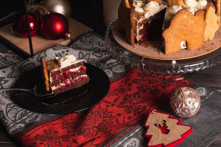 Cherry Cake Black forest on a dark background, decorated with gingerbread cookies with a cut piece on a serving plateの写真素材