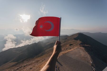 Turkey flag in a male hand against the backdrop of Taurus Mountains in sunset from a viewpoint of Tahtali Mountain. Tahtali Dagi, Antalya Province, Turkeyの写真素材