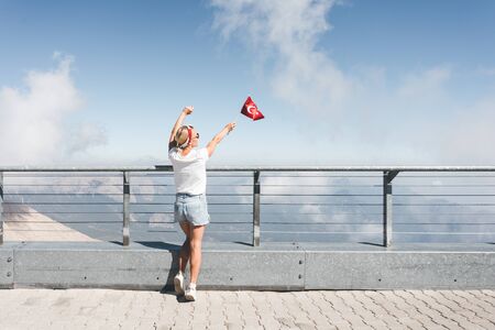 Young woman tourist stands on a viewing platform of Tahtali Mountain in Kemer with a red Turkey flag, Turkeyの写真素材