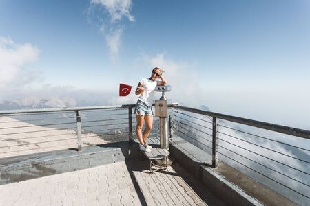 Young woman tourist stands on a viewing platform of Tahtali Mountain in Kemer with a red Turkey flag, Turkeyの写真素材