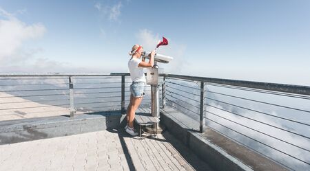 Young woman tourist stands on a viewing platform of Tahtali Mountain in Kemer with a red Turkey flag and looks in binoculars, Turkeyの写真素材