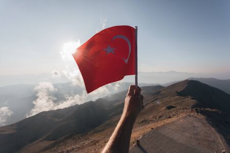 Turkey flag in a male hand against the backdrop of Taurus Mountains in sunset from a viewpoint of Tahtali Mountain. Tahtali Dagi, Antalya Province, Turkeyの写真素材