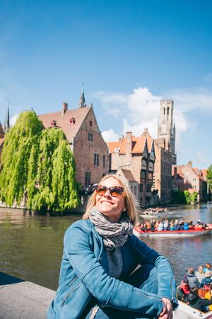 A beautiful young girl sits at the famous tourist spot with a canal in Bruges, Belgiumの写真素材