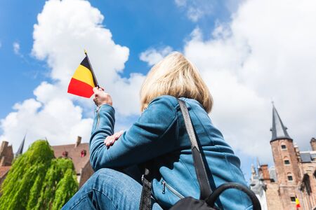Young woman tourist with the flag of Belgium in the hands is enjoying the views of the city in the historic center of Bruges near the famous viewport. Travel to Belgium.の写真素材
