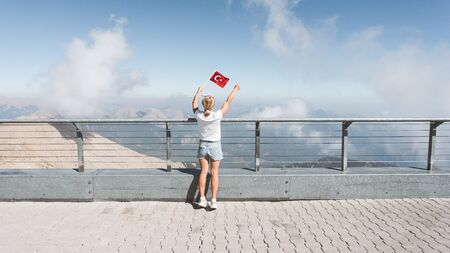 Young woman tourist stands with her back to the camera with the flag of Turkey in her hands on a fion of the mountains panorama.の写真素材