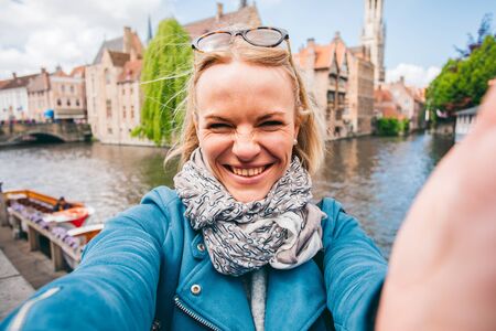 Beautiful young girl takes selfie photo of the famous tourist destination with a canal in Bruges, Belgiumの写真素材