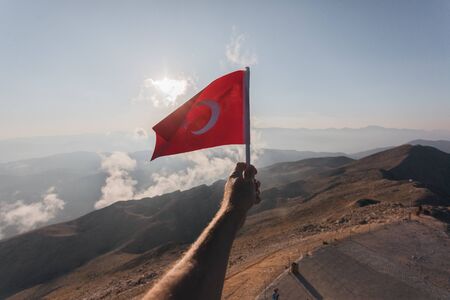 Turkey flag in a male hand against the backdrop of Taurus Mountains in sunset from a viewpoint of Tahtali Mountain. Tahtali Dagi, Antalya Province, Turkeyの写真素材