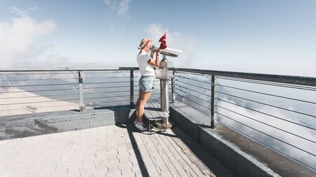 Young woman tourist stands on a viewing platform of Tahtali Mountain in Kemer with a red Turkey flag and looks in binoculars, Turkeyの写真素材
